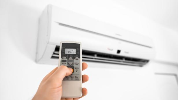 Hand holding remote control in front of the air conditioner.